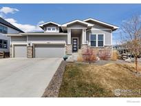 Charming gray home with a three-car garage, stone accents, manicured lawn, and covered front porch at 4877 Old River Ave, Firestone, CO 80504