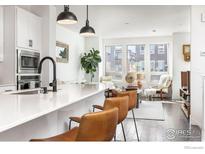 Bright open concept living room featuring modern white cabinets and a breakfast bar with brown leather barstools at 417 Promenade Dr, Superior, CO 80027