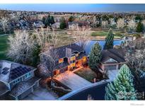Stunning aerial view of a beautiful home with a pond, golf course, and mature trees at twilight at 567 Manorwood Ln, Louisville, CO 80027