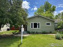 Charming green bungalow with well-kept lawn and mature trees under a blue sky with clouds at 117 Welch Ave, Berthoud, CO 80513