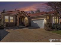 Charming single-story home featuring a red tile roof, stone accents, and a two-car garage under a colorful dusk sky at 2977 Dunes Ct, Longmont, CO 80503
