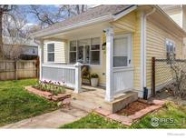Charming yellow home with a covered front porch, white railing, and a garden bed with tulips at 2121 Grove Cir, Boulder, CO 80302