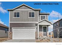 Charming two-story home featuring stone accents, a two-car garage, and gray woodgrain siding at 864 Leeward St, Lochbuie, CO 80603