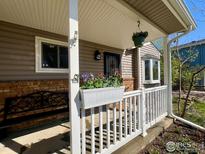 Charming front porch with a hanging flower basket and railing planter box with flowers at 1406 Oak Dr, Berthoud, CO 80513