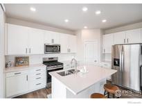 Modern kitchen with white cabinets, stainless steel appliances, quartz countertops, and an island with seating at 5805 Red Barn Ave, Mead, CO 80542