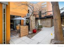Inviting outdoor patio featuring a table and chairs under a large umbrella, set against a brick wall and garden backdrop at 801 Confidence Dr # 2, Longmont, CO 80504
