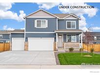 Two-story home features a blue exterior, stone accents, a two-car garage, and a well-manicured lawn at 262 Chardon Ave, Brighton, CO 80601