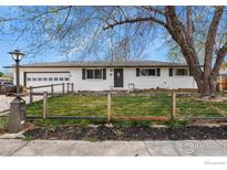 Charming single story home with a white brick exterior, black trim, attached garage, and a wood and wire fence at 440 Fox St, Longmont, CO 80504