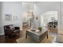 Bright living room with hardwood floors, curved staircase, and chandelier, and dining room beyond at 520 Campo Way, Superior, CO 80027