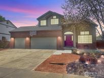 Charming two-story home featuring a three-car garage, brick accents, and a basketball hoop, enhanced by a vibrant twilight sky at 5832 E Wetlands Dr, Frederick, CO 80504