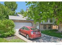 Charming brick home with an attached garage, green lawn, mature trees and a red car parked in the driveway at 13755 W 65Th Dr, Arvada, CO 80004