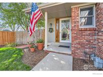 Inviting front porch with an American flag, flower pots, and a well-maintained brick and gray exterior at 12342 Milwaukee Ct, Thornton, CO 80241