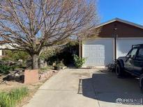 Home exterior featuring an attached two car garage and mature tree in the front yard at 1113 Lantern Dr, Fort Lupton, CO 80621