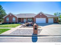 Charming brick home featuring a well-manicured lawn, rock water feature, and three-car garage at 2050 Emerald Dr, Longmont, CO 80504