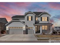 Beautiful two-story home featuring a three-car garage, covered porch, and manicured lawn at sunset at 904 Sundown Way, Erie, CO 80516