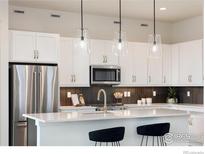 Modern kitchen with white cabinets, stainless steel appliances, and quartz countertops with elegant pendant lighting at 1581 Poplar Dr, Erie, CO 80516