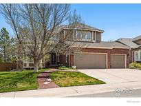 Inviting two-story home featuring a brick facade, three-car garage, and well-manicured lawn with mature trees at 10305 Charissglen Cir, Highlands Ranch, CO 80126