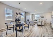 Open-concept living and dining area featuring modern lighting, fireplace, and wood-look flooring at 2732 Bear Springs Cir, Longmont, CO 80503