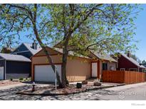 Cozy tan home featuring a two-car garage and a beautifully landscaped front yard with mature trees at 1072 Townley Cir, Longmont, CO 80501