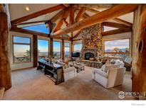 Spacious living room with exposed beam ceilings, large stone fireplace, and mountain views at 6553 Sunshine Canyon Dr, Boulder, CO 80302