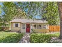 Charming yellow home with a red door, inviting front porch, and mature trees at 1136 Venice St, Longmont, CO 80501