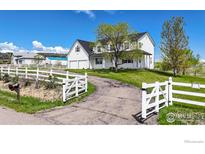 Charming two-story farmhouse-style home with a well-manicured lawn, mature trees, and a white fence surrounding the property at 5306 Foothills Dr, Berthoud, CO 80513