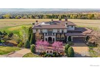 A stunning stucco home featuring a tile roof, porte-cochere, and lush landscaping with mature trees at 6541 Legend Ridge Trl, Niwot, CO 80503