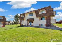 Charming two-story condo with brick accents and well-maintained lawn under a partly cloudy sky at 10211 Ura Ln # 104, Thornton, CO 80260