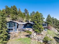 Mountain home featuring a deck with wood railings surrounded by mature trees and rocky landscape at 22598 Westview Ave, Golden, CO 80401