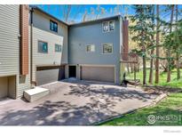 Multi-level home featuring a driveway leading to attached garages and a wooden walkway alongside the building at 4888 Silver Spruce Ln, Evergreen, CO 80439
