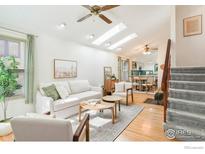 Bright living room featuring skylights, ceiling fan, hardwood floors, and open access to the kitchen and dining area at 821 Hayden Ct, Longmont, CO 80503