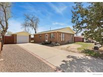 Charming brick home with a long driveway, detached garage, and mature trees, under a bright blue sky at 902 Pacific Pl, Fort Lupton, CO 80621