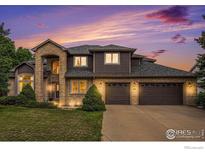 Beautiful two-story home with brick and brown siding, lush lawn and a three-car garage at dusk at 13971 Telluride Dr, Broomfield, CO 80020