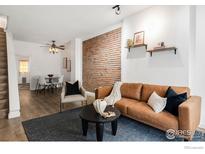 Inviting living room featuring a stylish leather sofa, brick accent wall, and open dining area with wood floors at 135 E 8Th Ave, Denver, CO 80203