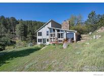 Charming exterior of home with a stone chimney, expansive windows, and inviting deck nestled in a wooded setting at 100 Wildcat Ln, Boulder, CO 80304