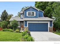 Charming two-story blue home featuring a well-manicured lawn, blue garage door, and lovely landscaping at 823 Timothy Dr, Longmont, CO 80503