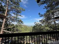 A scenic view from the deck showcasing lush trees and distant mountains against a bright, blue sky at 335 Wild Horse Cir, Boulder, CO 80304