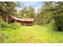Charming log cabin-style home with a stone chimney and a lush, green lawn surrounded by trees at 35106 Boulder Canyon Dr, Boulder, CO 80302