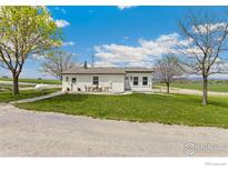 Charming single-story home with white exterior, front yard, and outdoor seating area on the patio at 19810 County Road 1, Berthoud, CO 80513