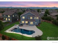 Beautiful backyard with a large in-ground pool, hot tub, green lawn, and mountain views at dusk at 13598 Horseshoe Cir, Mead, CO 80542
