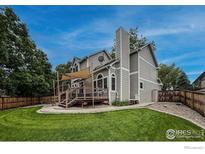 Expansive backyard featuring a large deck, lush green lawn, mature trees, and a private fenced in yard at 6255 Collegiate Dr, Highlands Ranch, CO 80130