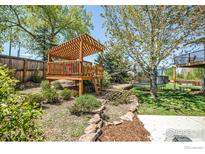 Beautiful backyard with a wooden playhouse, lush landscaping, and mature trees at 1067 W Alder St, Louisville, CO 80027