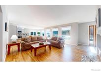 Bright and airy living room featuring hardwood floors and comfortable seating by the large windows at 6260 Rain Dance Trl, Littleton, CO 80125