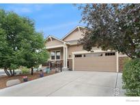 Inviting tan two-story home featuring a two car garage, a welcoming front porch, and manicured landscaping at 2124 Addie Rose Ln, Longmont, CO 80501