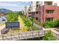 View of condos with brick and light-colored siding, landscaped grounds, and a walking bridge, with a mountain view in the background at 3301 Arapahoe Ave # 216, Boulder, CO 80303