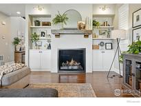 Cozy living room featuring a fireplace with decorative shelving and hardwood floors at 952 Pinecliff Dr, Erie, CO 80516