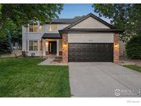 Charming two-story home showcasing a manicured lawn, brick accents, and a black garage door at 10216 Sandy Ridge Ct, Firestone, CO 80504