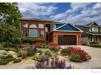 Inviting brick two-story home featuring a landscaped front yard filled with colorful flowers and mature trees at 3142 Captains Ln, Longmont, CO 80503