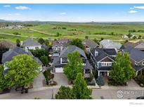 An aerial view of a home with a well-maintained lawn and landscaping overlooking a green field and distant mountains at 1043 Terrace S Cir, Boulder, CO 80304