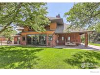 Expansive rear exterior view with a brick facade, porch with a swing, and lush green lawn at 7975 Anchor Dr, Longmont, CO 80504